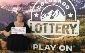 Shellie R. holding an oversized check for $1,000 in front of Colorado Lottery background