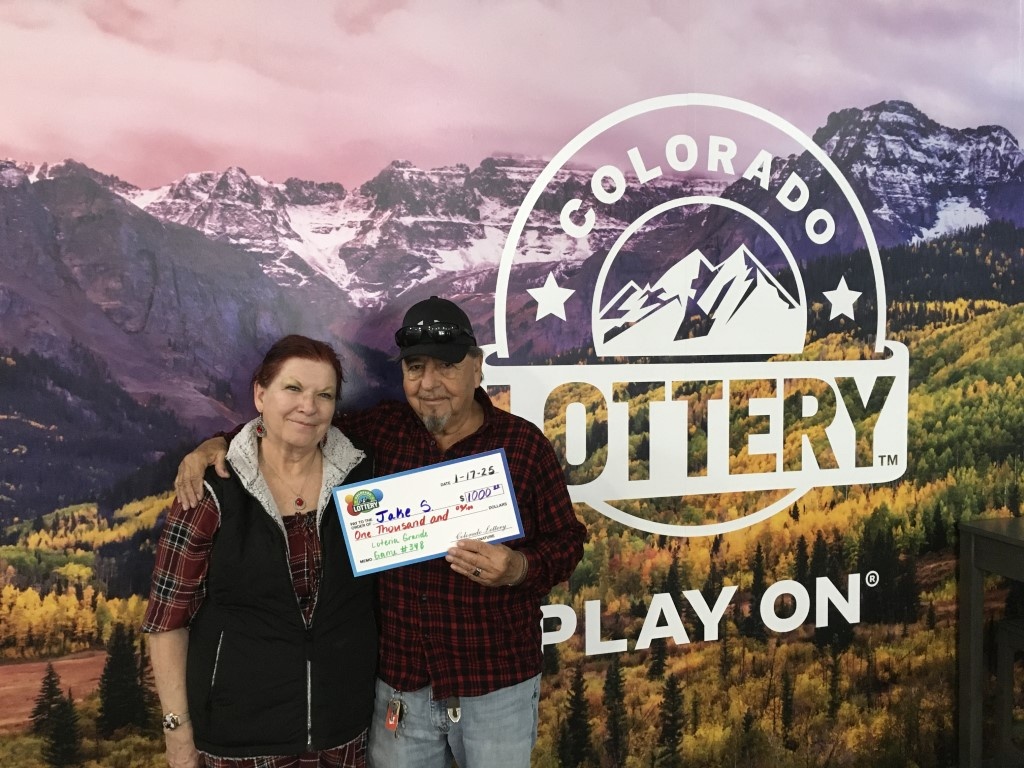 Jake S. sosteniendo un cheque por $1,000 frente a un fondo de la Lotería de Colorado.