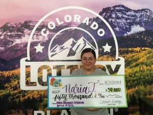 Naria J. sosteniendo un cheque de gran tamaño por $50,000 frente al fondo de la Lotería de Colorado