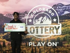 Deonte V. holding an oversized check for $100,000 in front of Colorado Lottery background