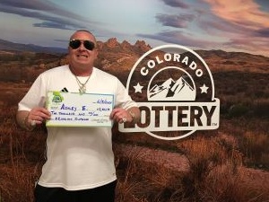 Ashley E. sosteniendo un cheque gigante de $2,500 frente al fondo de la Lotería de Colorado.