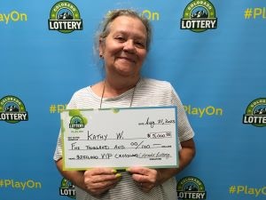 Kathy W. of Denver holding an oversized check for $5,000 in front of Colorado Lottery background.