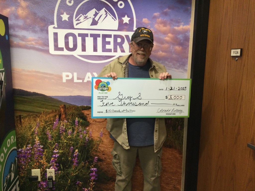 Guy S. sosteniendo un cheque por $5,000 frente a un fondo de la Lotería de Colorado.