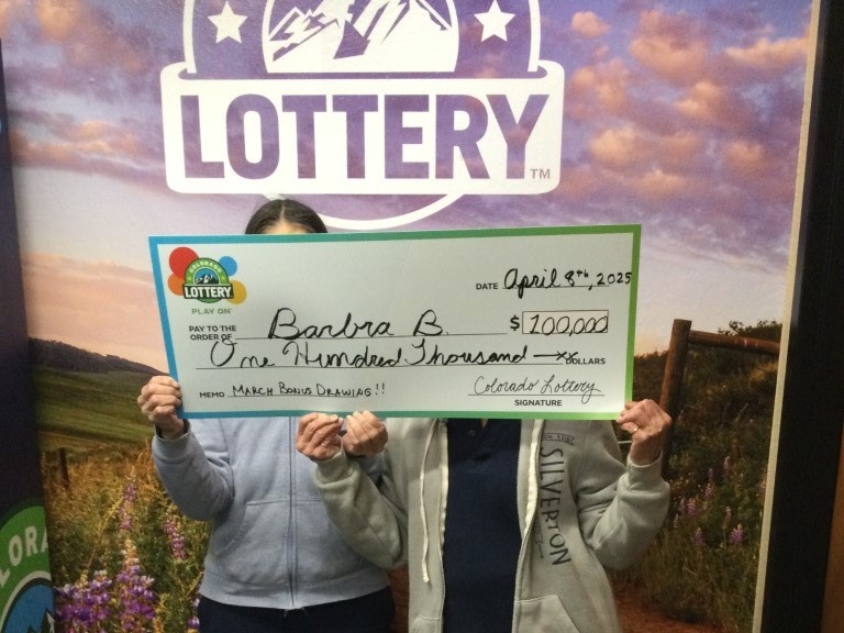 Ganador sosteniendo un cheque de gran tamaño en la oficina de reclamos de la Lotería de Colorado.
