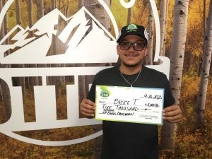Bruce T. de Fort Worth, Texas, sosteniendo un cheque de gran tamaño por $5,000 frente al fondo de la Lotería de Colorado