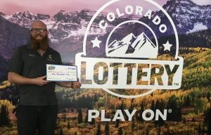 Curren C. de Calhan sosteniendo un cheque de gran tamaño por $1,000 frente al fondo de la Lotería de Colorado.