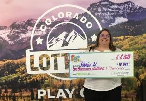 Jennifer W. de Pueblo sosteniendo un cheque de gran tamaño por $10,000 frente al fondo de la Lotería de Colorado.