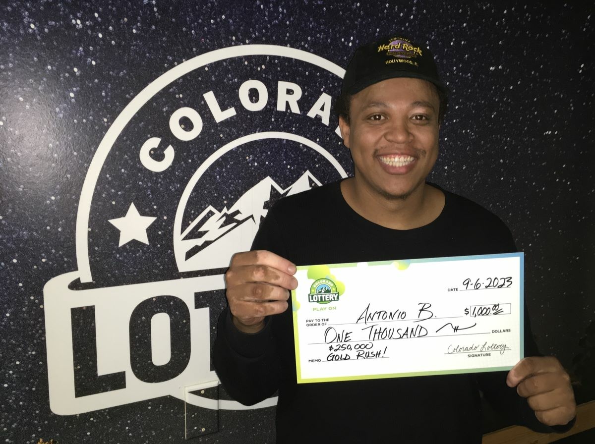 Antonio B. of Aurora holding an oversized check for $2,000 in front of Colorado Lottery background.