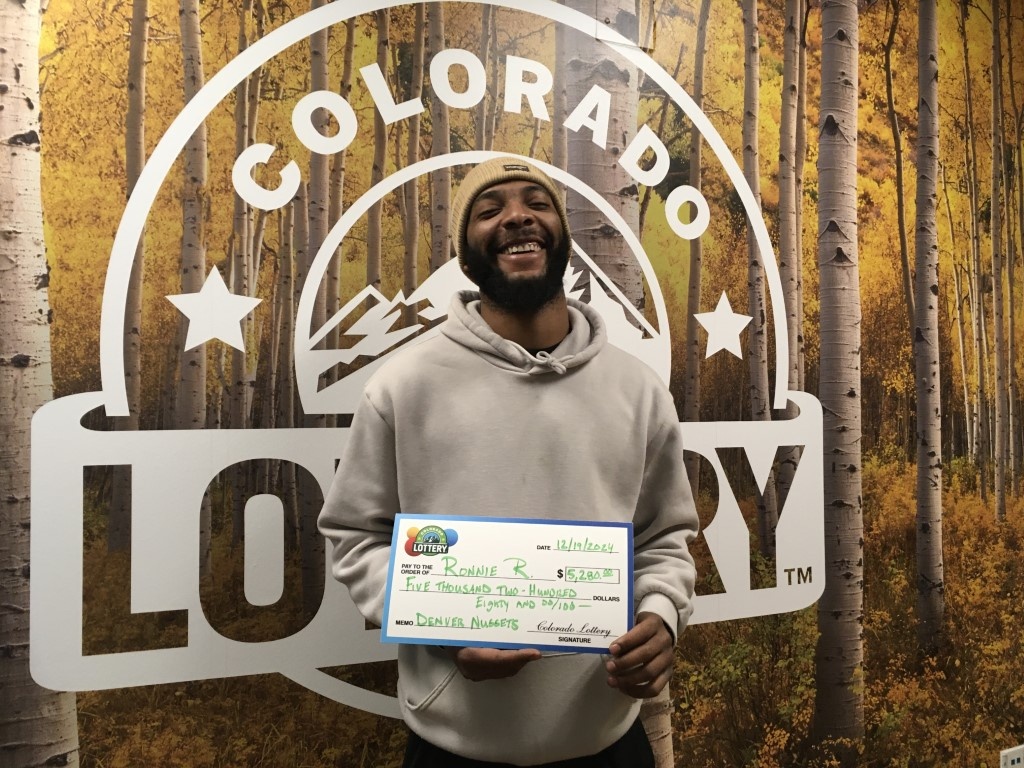 Ronnie R. sosteniendo el cheque gigante de $5,280 frente al fondo de Colorado Lottery