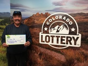 Dell G. holding check for $2,000 in front of Colorado Lottery background