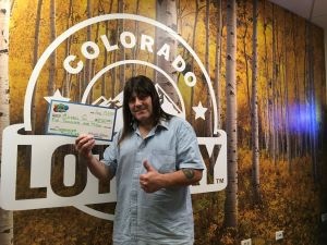 Michael C. holding an oversized check for $5,000 in front of Colorado Lottery background