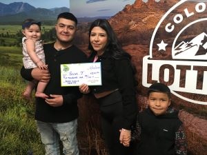 Selyna J. sosteniendo el cheque gigante de $20,000 frente al fondo de Colorado Lottery