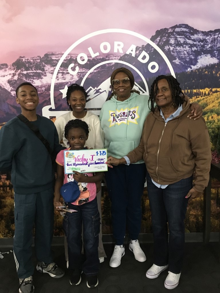 Vicky J. sosteniendo un cheque por $2.500 frente a un fondo de la Lotería de Colorado.