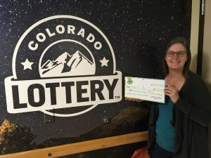 Kelli S. de Highlands Ranch sosteniendo un cheque de gran tamaño por $1,000 frente al fondo de la Lotería de Colorado
