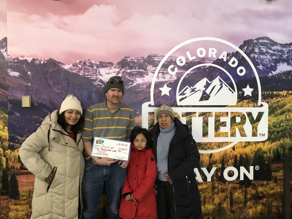 El ganador sostiene un cheque de gran tamaño frente a un fondo de la Lotería de Colorado