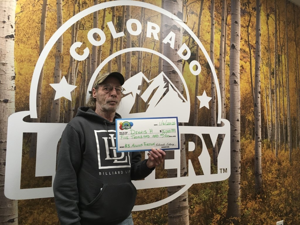 Dennis H. sosteniendo un cheque por $5,000 frente a un fondo de la Lotería de Colorado.