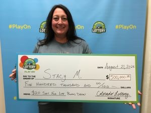 Stacy M. de Commerce City sosteniendo un cheque de gran tamaño por $ 500,000 frente al fondo de la Lotería de Colorado.