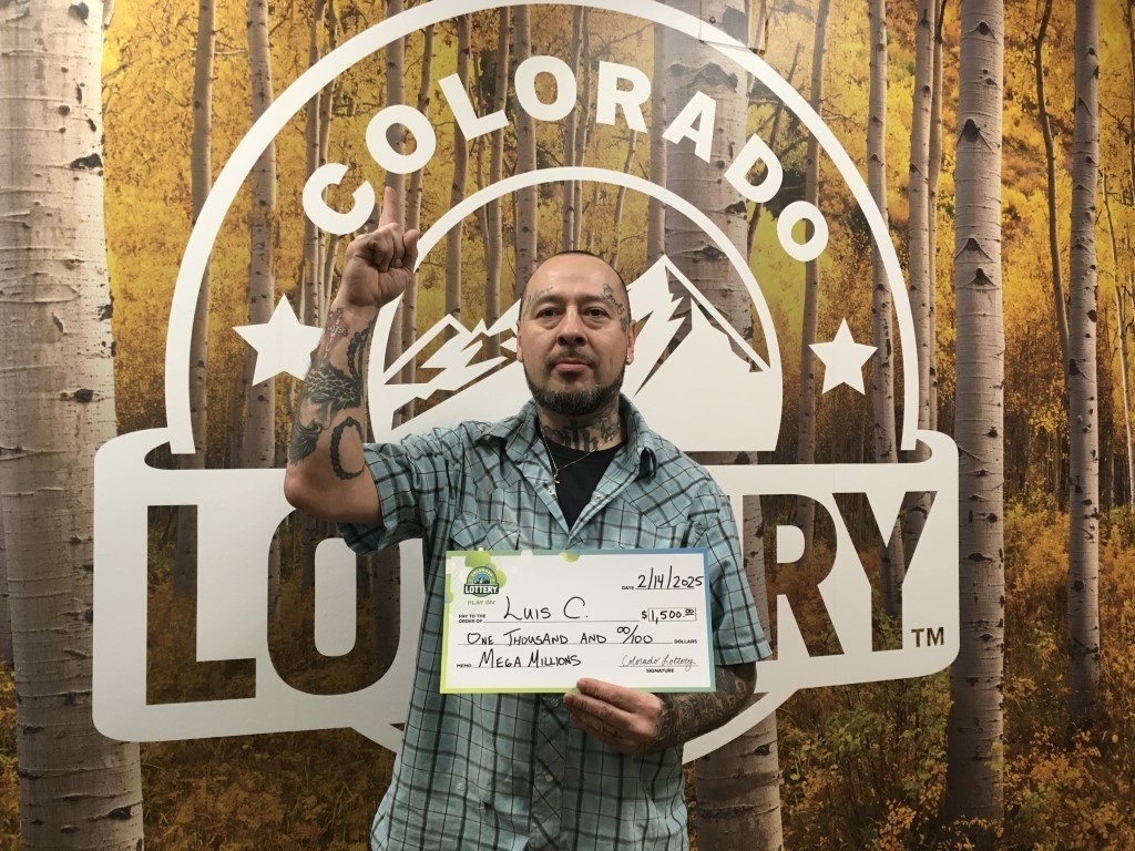 El ganador sostiene un cheque de gran tamaño frente a un fondo de la Lotería de Colorado