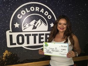 Tiffany B. de Westminster sosteniendo un cheque de gran tamaño por $1,000 frente al fondo de la Lotería de Colorado.
