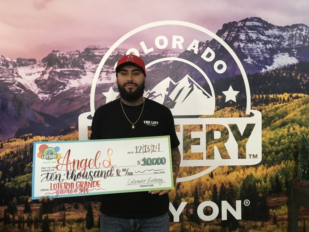 Angel S. sosteniendo el cheque gigante de $10,000 frente al fondo de Colorado Lottery