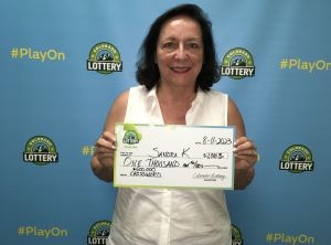 Sandra K. de Lakewood sosteniendo un cheque de gran tamaño por $1,000 frente al fondo de la Lotería de Colorado.