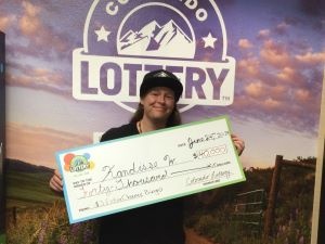 Kandisse W. holding an oversized check for $40,000 in front of Colorado Lottery background