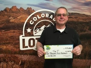 Tim P. sosteniendo el cheque gigante de $2,500 frente al fondo de Colorado Lottery