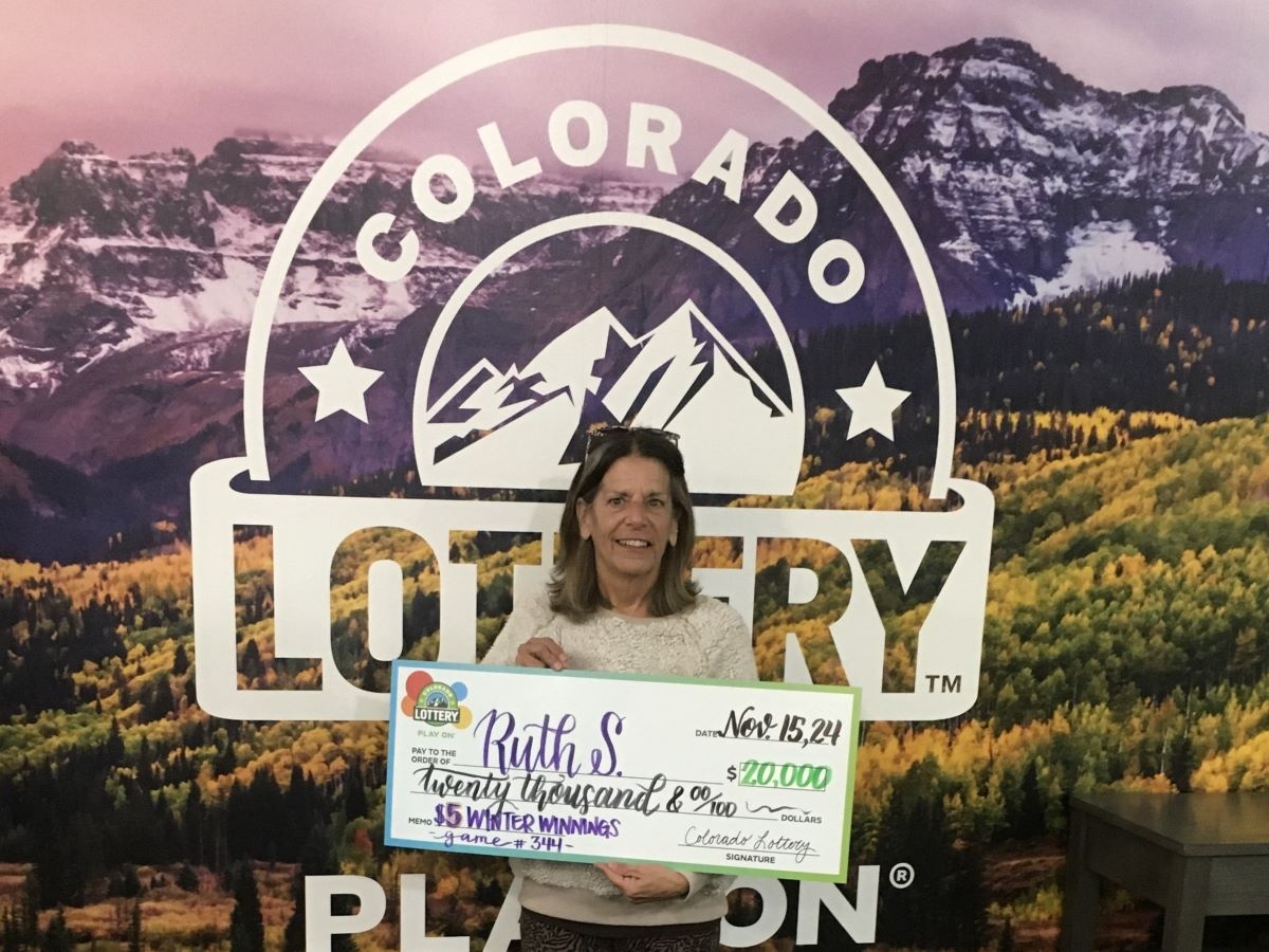 Ruth S. sosteniendo el cheque gigante de $20,000 frente al fondo de Colorado Lottery