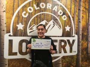 Irene B. sosteniendo el cheque gigante de $1,000 frente al fondo de Colorado Lottery