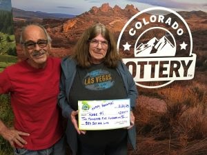 Rose M. sosteniendo su cheque de gran tamaño por $2,500 frente al fondo de la Lotería de Colorado
