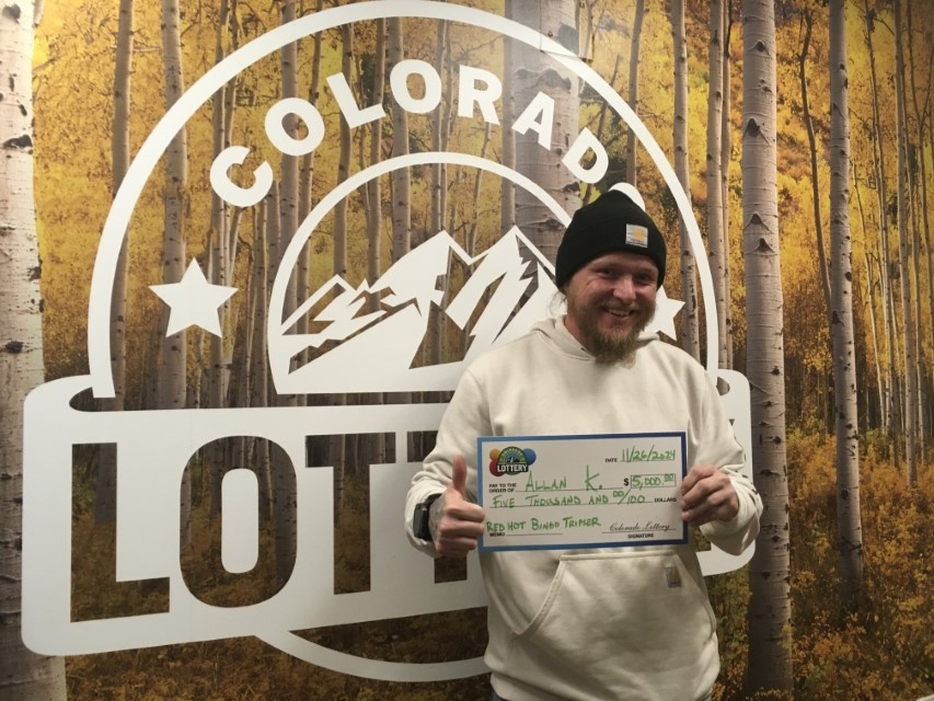 Allan K. sosteniendo el cheque gigante de $5,000 frente al fondo de Colorado Lottery