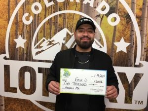Erik D. holding an oversized check for $1,000 in front of Colorado Lottery background