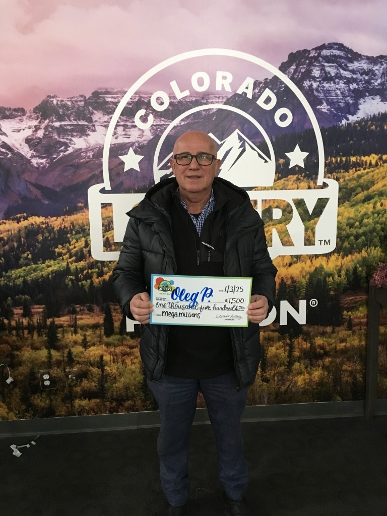 Oleg P. sosteniendo un cheque por $1,500 frente a un fondo de la Lotería de Colorado.
