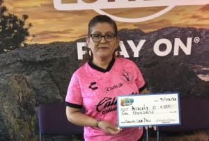 Aracely O. of Greeley holding an oversized check for $1,000 in front of Colorado Lottery background.