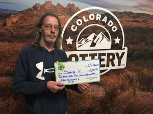 Dennis H. holding an oversized check for $2,500 in front of Colorado Lottery background