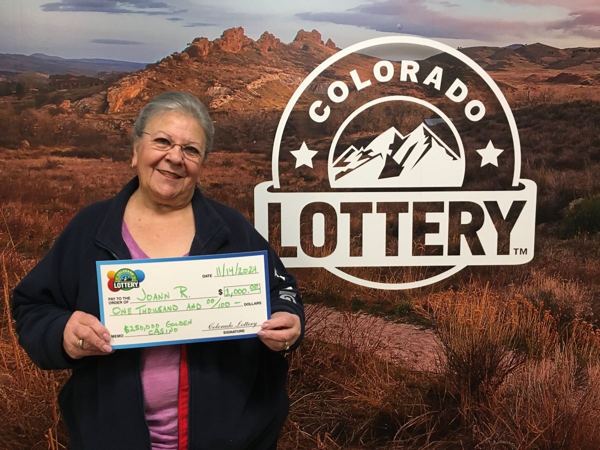 Joann R. holding an oversized check for $1,000 in front of Colorado Lottery background
