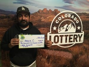 Kermis C. sosteniendo el cheque gigante de $2,500 frente al fondo de Colorado Lottery
