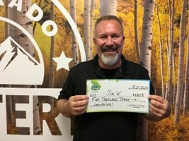 Jim W. of Littleton holding an oversized check for $5,003 in front of Colorado Lottery background.