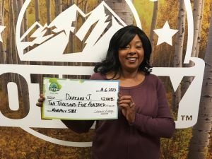 Dakeana J.  holding an oversized check for $2,500 in front of Colorado Lottery background