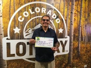 Ricardo Z. holding an oversized check for $1,012 in front of Colorado Lottery background