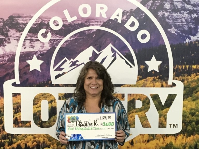 Christine R. sosteniendo un cheque gigante frente al fondo de la Lotería de Colorado