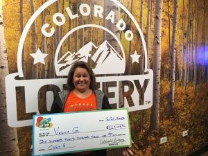Virginia G. holding her oversized check for $2,500 in front of Colorado Lottery background