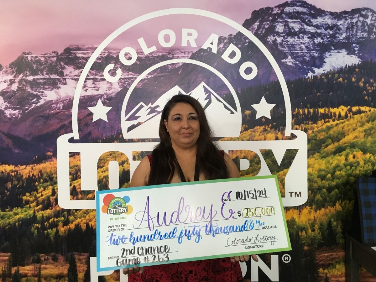 Audrey E. holding oversized check for $250,000 in front of Colorado Lottery background