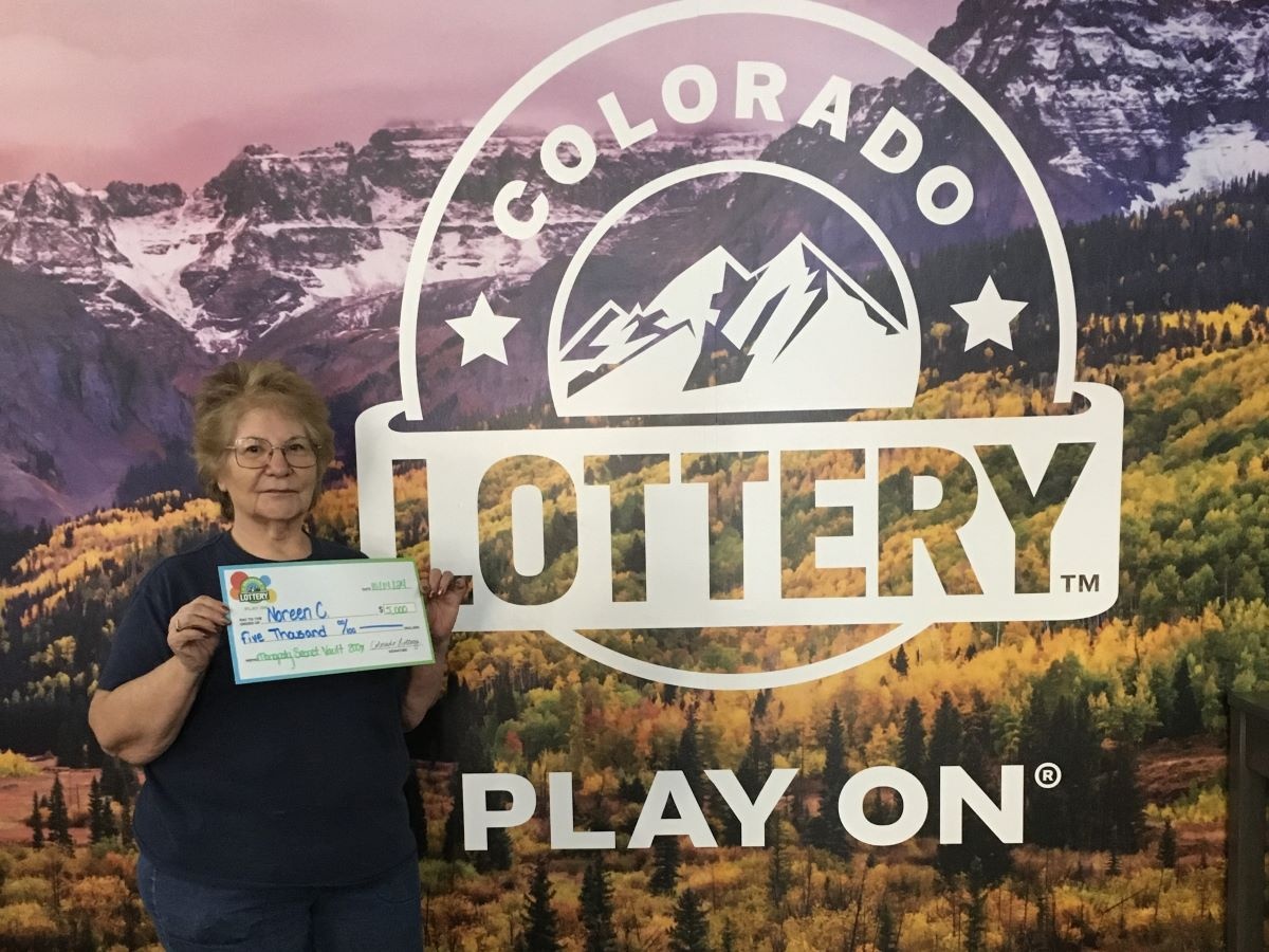 Noreen C. holding an oversized check for $5,000 in front of Colorado Lottery background