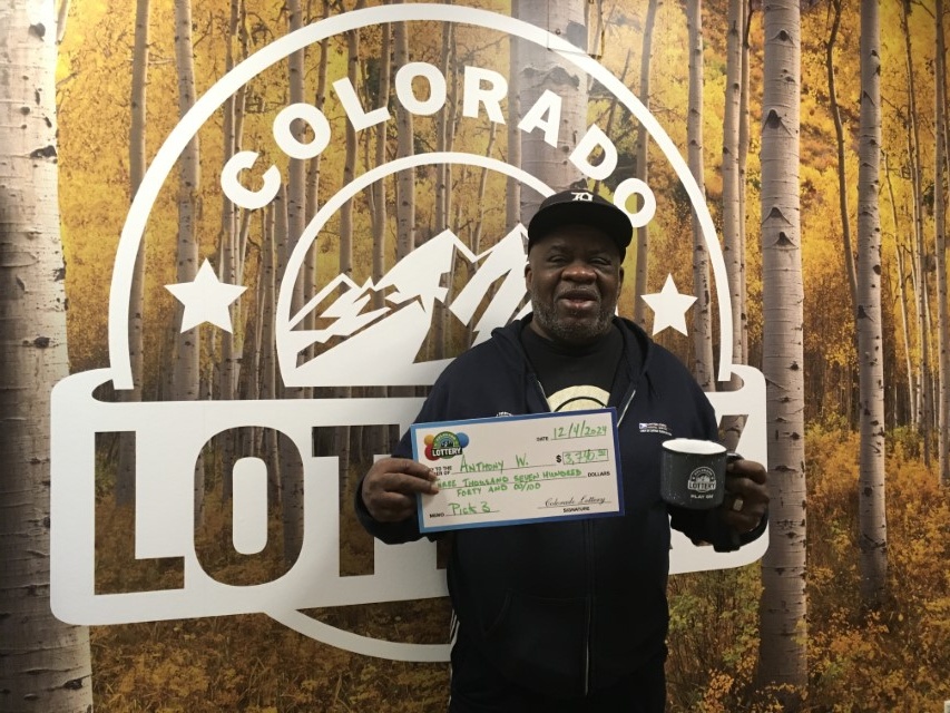 Anthony W. sosteniendo el cheque gigante de $3,740 frente al fondo de Colorado Lottery